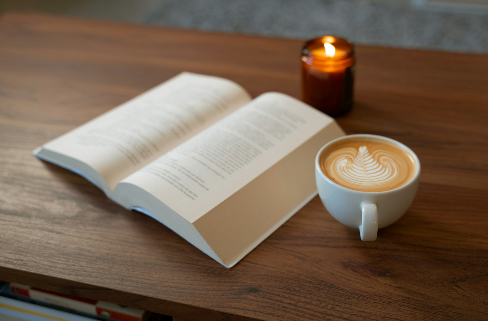 An open book, a latte, and a candle on a wooden table